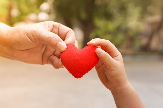 Symbolfoto für die Ambulante Hilfe - Sucht, eine keine und große Hand halten gemeinsam ein Herz aus rotem Stoff