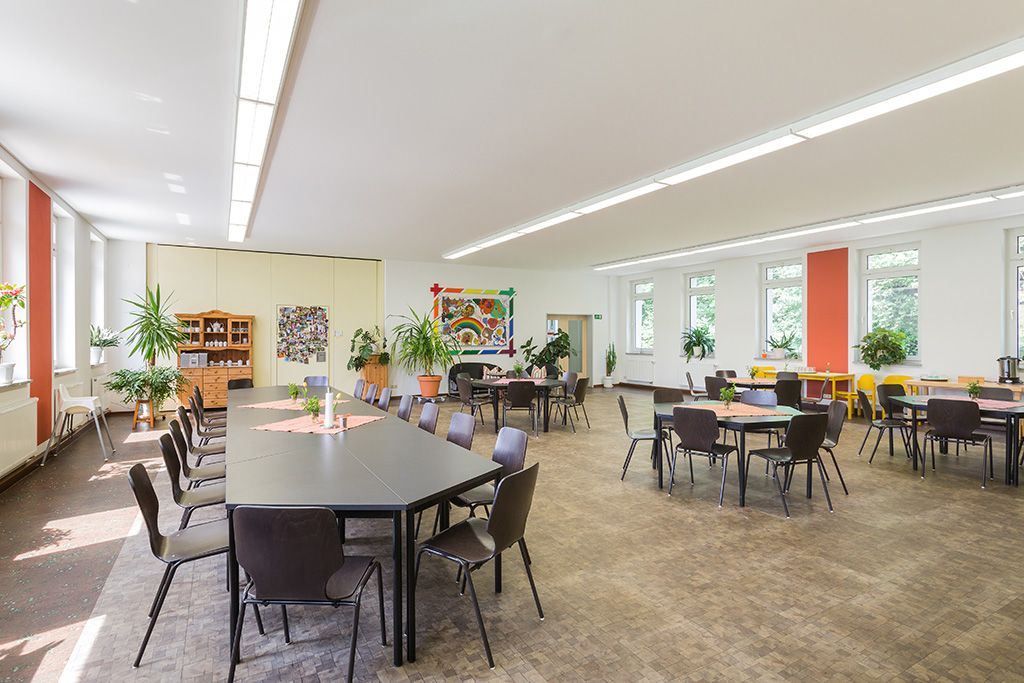 Der großzügige lichtdurchflutete Gemeinschaftsraum im Suchthilfezentrum für Mutter und Kind in Wolfersdorf. Die dunklen Tischgruppen mit passenden Stühlen bieten mindestens 30 Personen Platz.