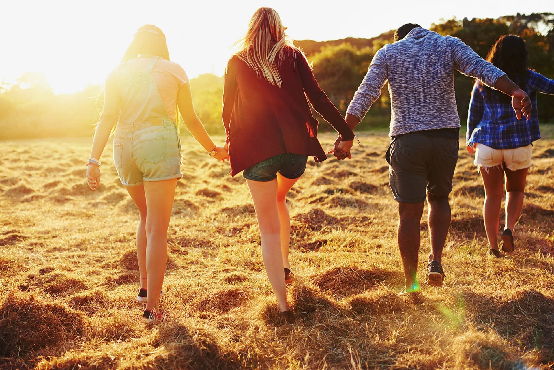 Symbolfoto für FSJ und BFD: Junge Menschen von hinten gehen Hand in Hand der Sonne entgegen