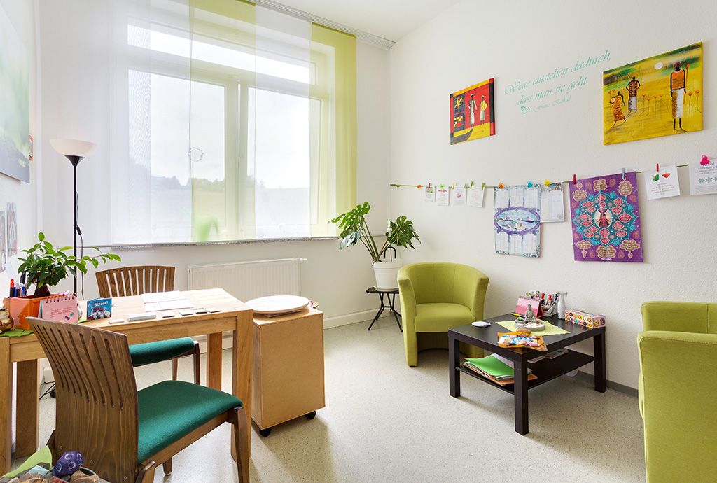 Blick durch die Tür in ein freundlich gestaltetes helles Besprechungszimmer im Suchthilfezentrum für Mutter und Kind in Wolfersdorf. Das Zimmer wirkt durch die warmen Farben und vielen Bilder an der Wand sehr gemütlich.