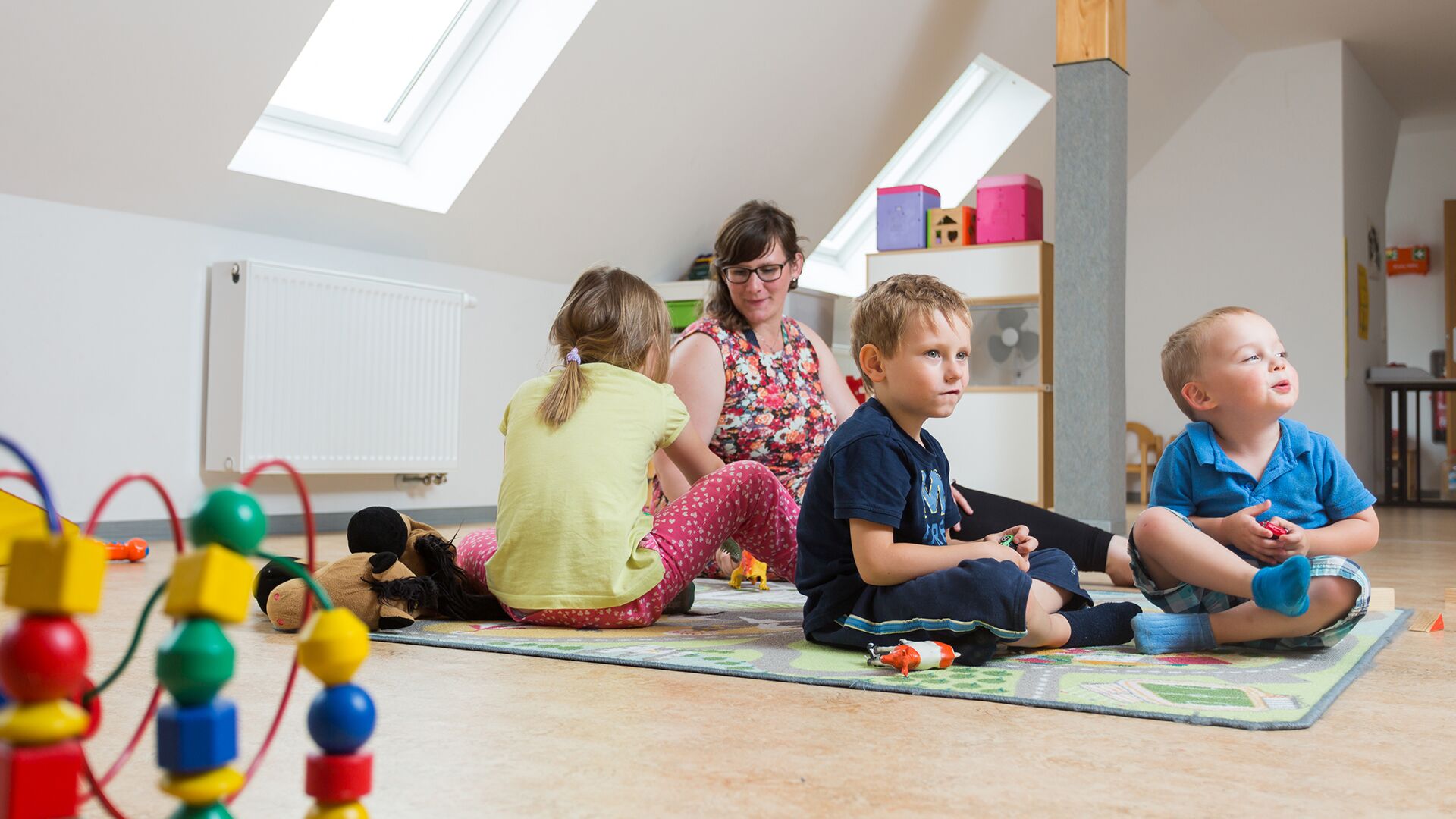 Praktikantin mit Kleinkindern auf Spieleteppich