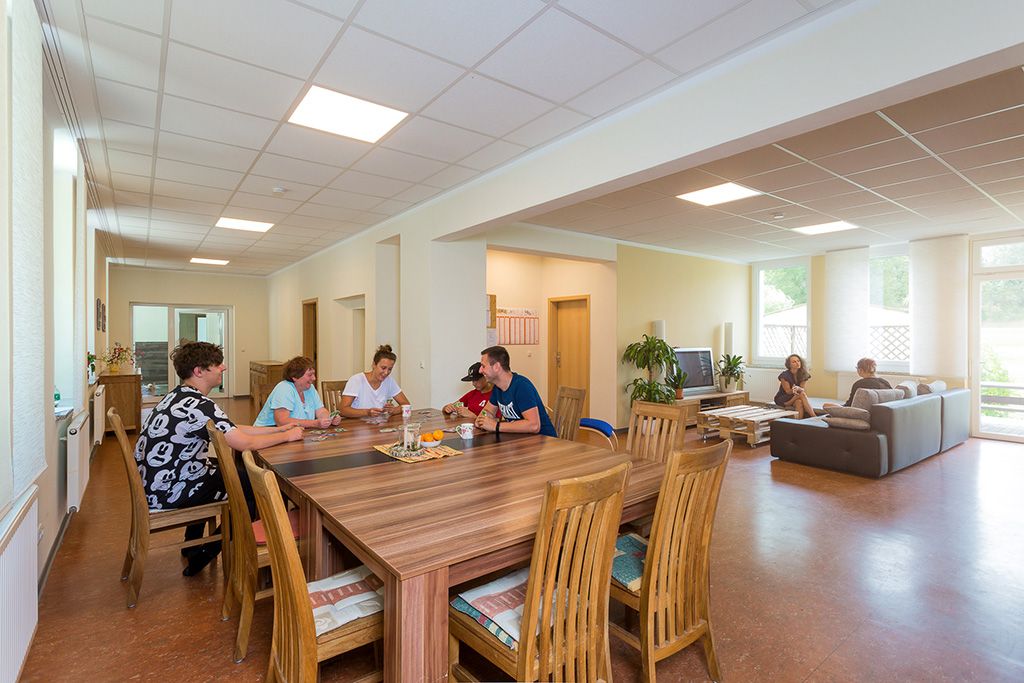 Gemeinschaftsraum der neu renovierten Wohngruppe: Erzieher und Jugendliche in fröhlicher Stimmung spielen am großen Holztisch Karten.